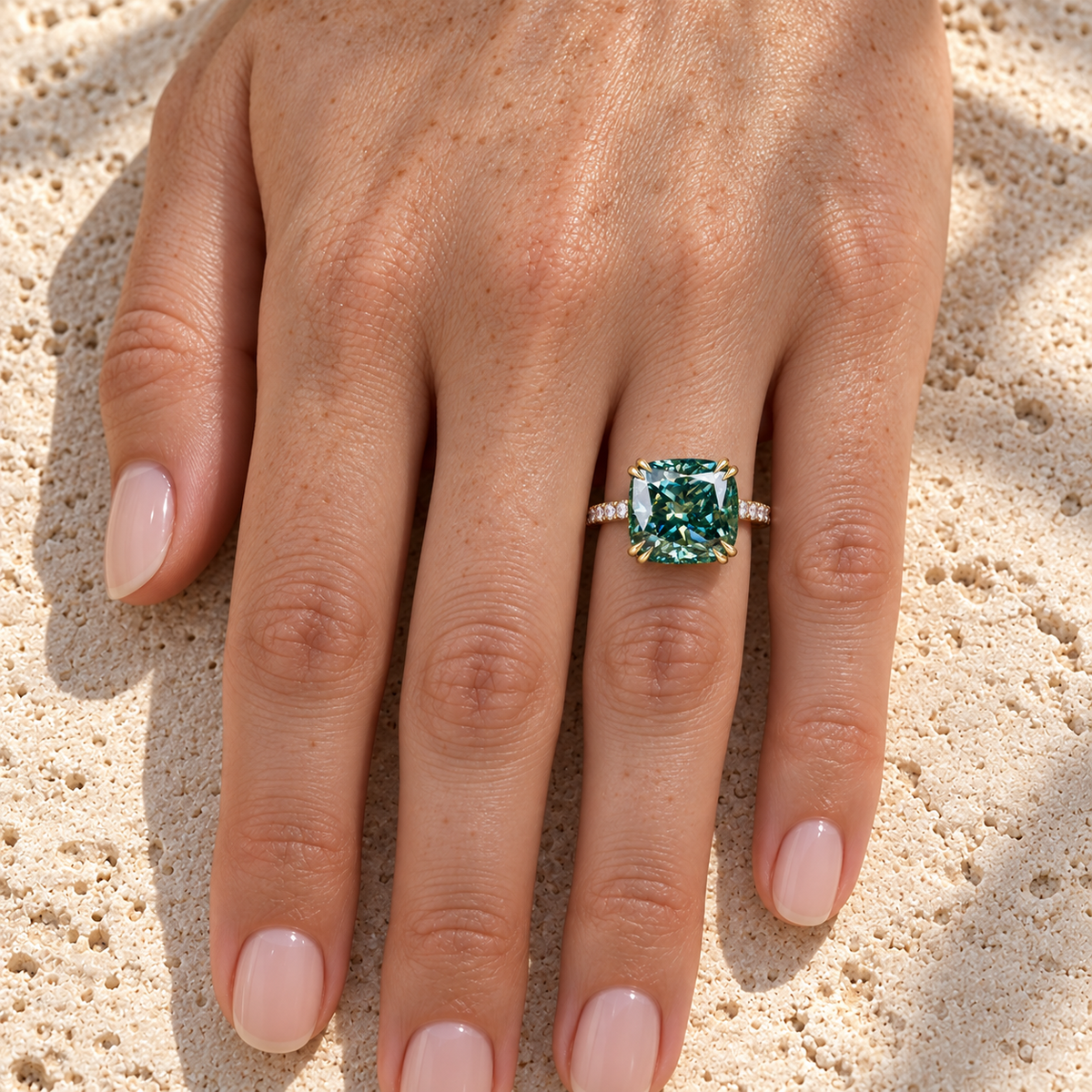 Greenish blue cushion moissanite engagement ring worn on the hand