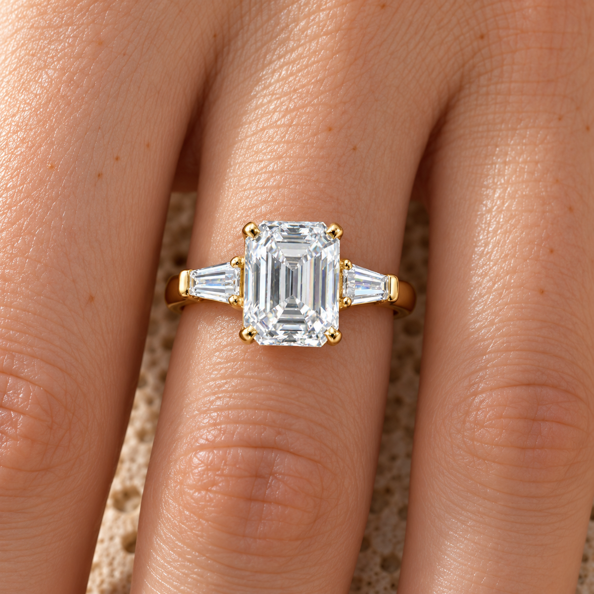 Emerald cut three stone moissanite ring in yellow gold worn on the hand